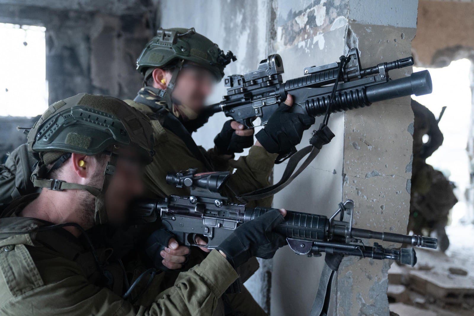 Two Israeli soldiers with faces blurred aim rifles from inside a damaged building during ground operations in the Gaza Strip, April 2025.