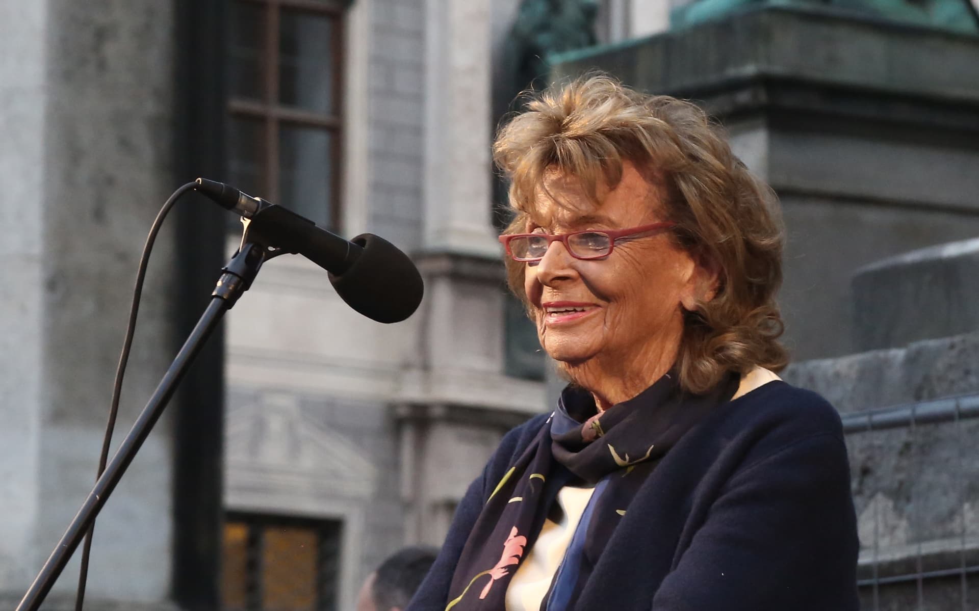 Charlotte Knobloch, president of the Jewish community of Munich and Upper Bavaria, smiling at a microphone in front of a stone facade at a solidarity rally in Munich, October 9, 2023.
